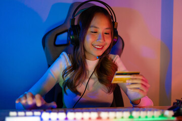Top up online game with credit card concept. Gamer and E-Sport online of Asian woman playing online computer video game with lighting effect, broadcast streaming live at home. Gamer and E-Sport gaming
