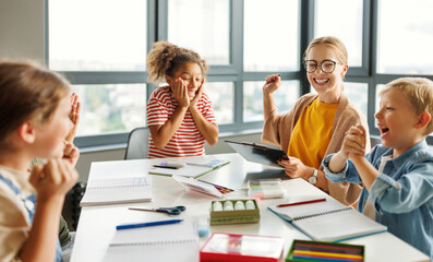 Teacher and joyful students celebrate   successful completion of collective school work in a bright...