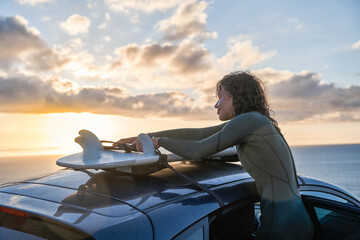 Curly young woman taking surfboard from her car and preparing for the training