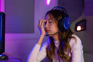 Eyes tired. Gamer and E-Sport online of Asian woman playing online computer video game with lighting effect, broadcast streaming. Her eyes were tired from staring at the screen for a long time. © Kiattisak