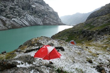 Red tent on bank of Lake Ala-Köl (Ala-kol, Ala-kul) in Tien Shan mountains in west of Kyrgyzstan, Asia. Tent is covered with snow a bit. Touristic destination for trekking.