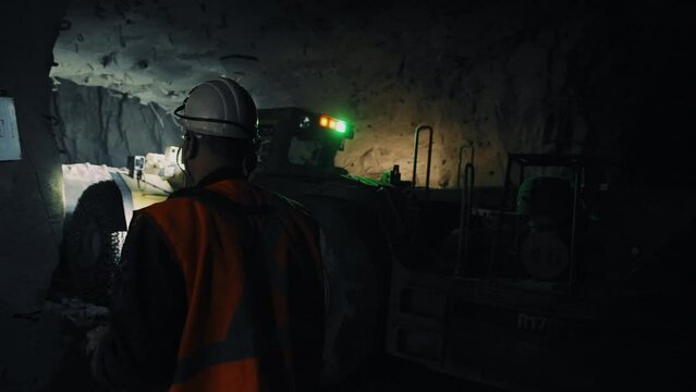 Mining ore underground in the dark. Excavator collects ore. A worker in a helmet controls the machine. Mining process. 4K