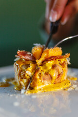 Frittatina di pasta fritta al gusto Carbonara mentre viene tagliata a metà e con sopra un tuorlo d'uovo e bacon croccante