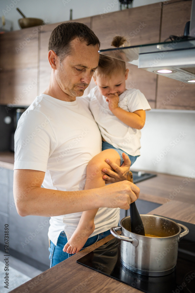 Wall mural Father with his daughter on his hands cooking soup together in modern home kitchen