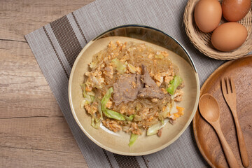 Stir fried vermicelli with pork, egg and collard greens in a white plate.