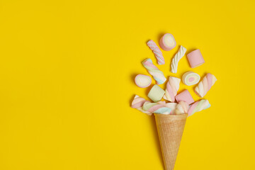 Colorful marshmallows with icecream cone on yellow background with copy space. Creative minimal sweet holiday concept