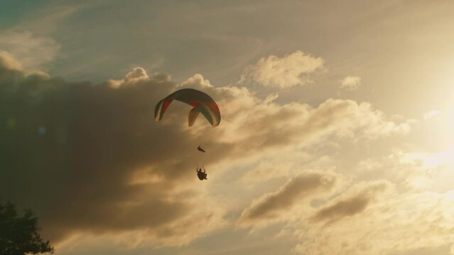 Two paragliders soar in a beautiful golden sky against the sunset. Parachutes or paragliding experience. Extreme sport on a paraglider with a parachute flying against a bright sunny sunset,