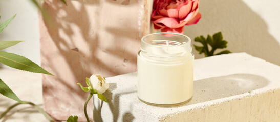 Composition with aromatic candle in jar on concrete podium. Mockup soy wax candle in natural style with flower. Scented handmade candle with wick.  Handmade spa product  from soy wax in glass.
