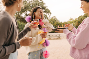 Fototapeta premium Cheerful young caucasian ladies enjoy spending time on holiday in honor of friend nature. Brunettes drink drinks, wear sweaters. Lifestyle concept
