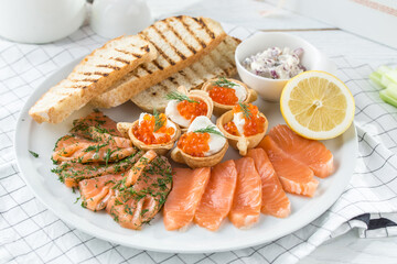 Fish plate with different types of smoked and salted fish, lemon and toasted bread on the table