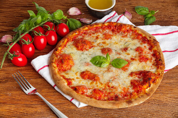 Thin pizza with tomato sauce, cheese and basil on a wooden background
