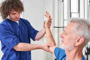 Retirement man receiving massage by male physic therapist of his arm due to injury