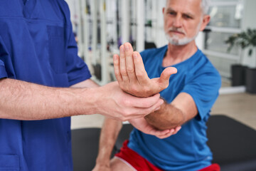 Obraz premium Senior man receiving massage by male physic therapist of his arm due to injury