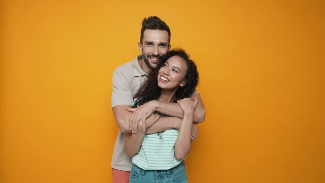Lovely brunette couple hugging and looking at the camera in the yellow studio