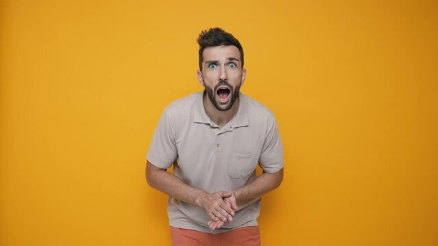 Surprised brunet man wearing t-shirt rejoicing and looking at the camera in the yellow studio