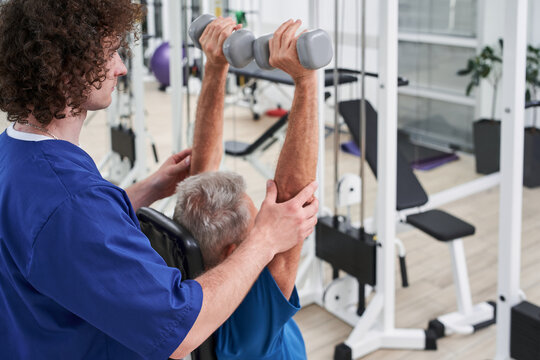 Senior man performing hands exercises assisted by certified physiatrist at the hospital