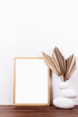 White frame mockup with dry palm leaves in a vase on wooden table