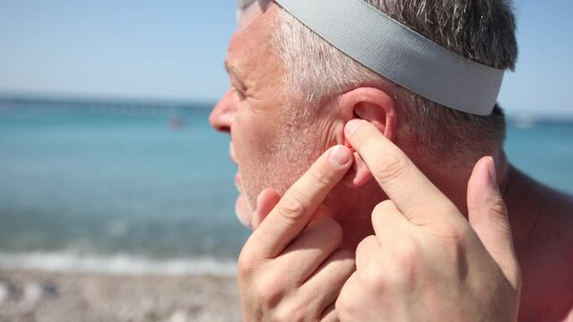 Mature man putting silicone ear plugs, surfers earplugs, swim plugs