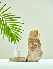 Podium of marble stones with mockup plastic jar, green palm leaf. Presentation of natural dietary...