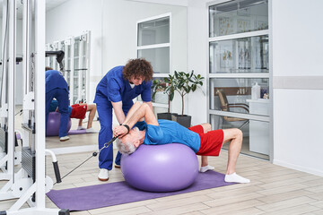 Retirement man training arms with trx fitness straps in the gym with coach’s help