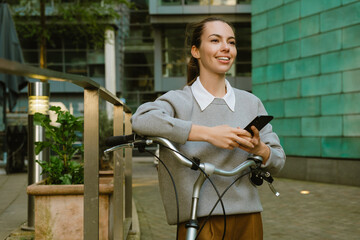 Fototapeta na wymiar Young businesswoman using cellphone standing by bicycle on street