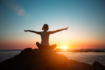 Silhouette women do yoga, meditate on the ocean during sunset.
