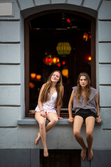 Two pretty girls sitting on the window of a nightclub.
