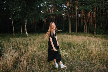 beautiful young girl in black dress and with long hair is resting in nature