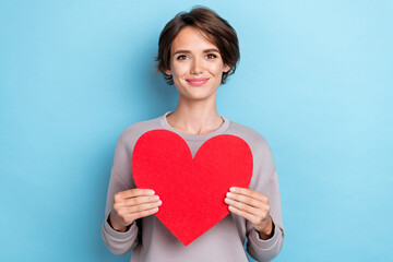 Portrait of lovely adorable girl with short hairstyle wear gray sweatshirt holding big red heart in arms isolated on blue color background