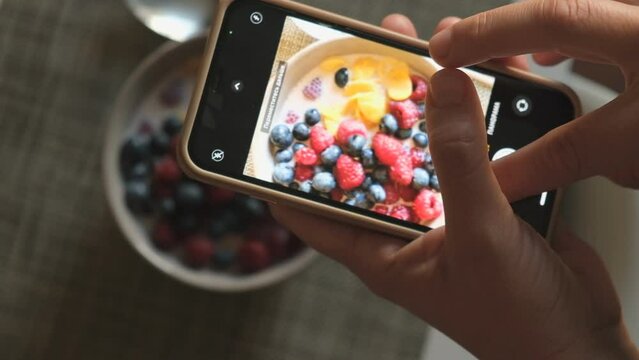A man takes a picture of a bowl of fresh and appetizing food on the table. Filming food with a smartphone.