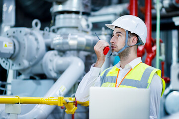 Engineer industrial plant with a laptop in hand, Engineer looking of working at industrial machinery setup in factory.
