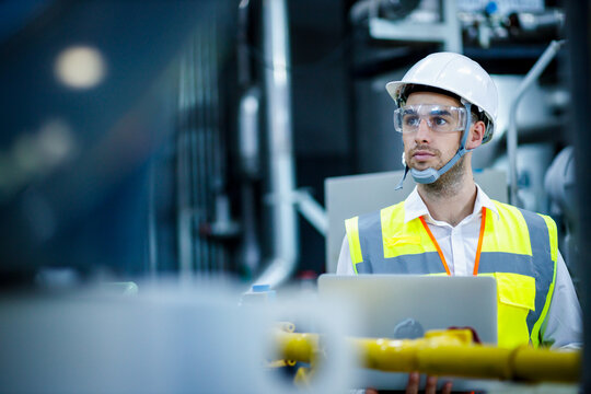 Engineer industrial plant with a laptop in hand, Engineer looking of working at industrial machinery setup in factory.