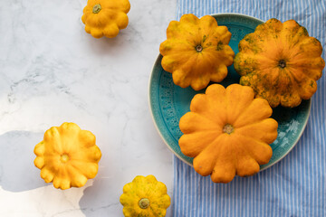 Yellow patisson, pattypan scallop squash vegetable on blue plate on white marble table background. Top view, flat lay. Autumn, fall harvest concept	