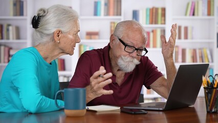 Elderly couple home finances, reviewing their bank money accounts using laptop stressful emotion at home