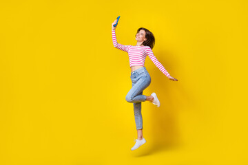 Fototapeta na wymiar Full body photo of nice young lady jump make selfie front camera hold gadget wear stylish striped look isolated on yellow color background