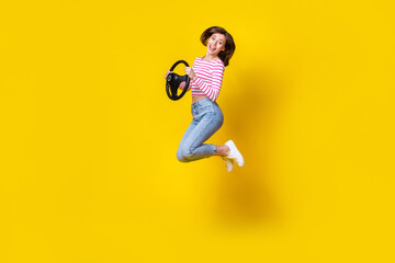 Fototapeta na wymiar Full length photo of cute gorgeous impressed girl brunette hair wear jeans jumping hold steering wheel isolated on yellow color background
