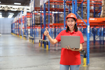 Portrait of warehouse workers young asian woman standing and using computer while showing thumb up and controlling stock and inventory in retail warehouse logistics, distribution center