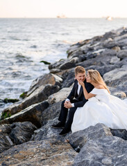 Young Couple Posing Against Sea, Sitting On Rocks