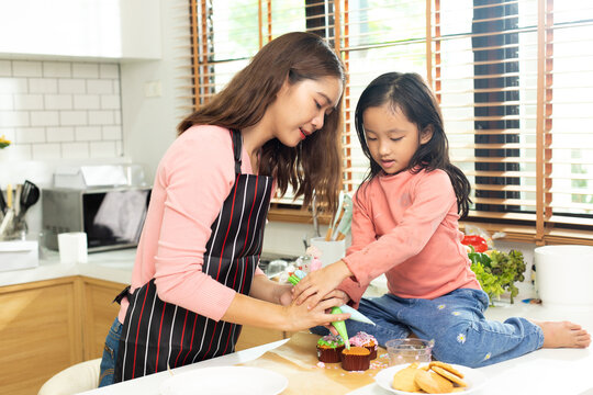 Asian Preschool Kid Person Make Cake Cooking In Kitchen, Mother Prepare Decoration Pretty With Fun Educate On Cupcake For Birthday Sister. Cream Mess All Over Hair Face Mouth, Feel Happy, Copy Space