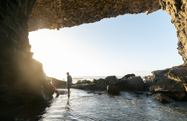 Young Couple on the Entrance of a Ocean Cave Against Sunlight over the Horizon.Copy Space