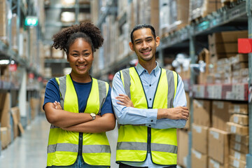 Naklejka premium Asian male and African American female employees wearing colleague uniforms standing with their arms crossed and proud of warehouse and freight service.