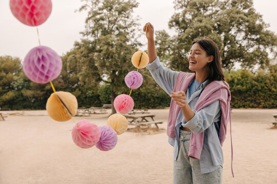 Cheerful young caucasian woman holding garlands enjoying spending time outdoors. Brunette smiles, wears sweatshirt and pants. Positive emotions concept