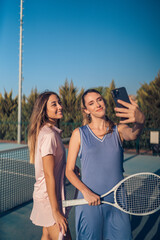 Dos chicas vestidas con ropa de tenis rosa y morada paseando juntas y haciendose selfies con smartphone en cancha de tenis