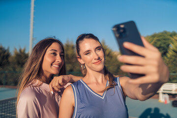 Dos chicas vestidas con ropa de tenis rosa y morada paseando juntas y haciendose selfies con...
