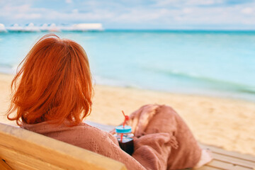 Woman is resting on the sea beach and admiring the ocean landscape. Red-haired girl from behind is...