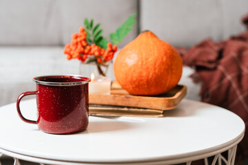 Still life book, candle, rowan berry, pumpkin and a cup of tea or coffee in the living room on a table, home decor in a cozy house. Autumn weekend concept, plaid. Fallen leaves and home decoration
