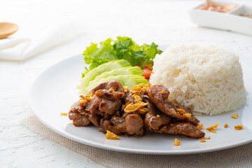 Close up Stir fried sliced Pork meat with Garlic and pepper with oyster sauce serve with cooked thai jasmine rice in white plate,popular Thai Street food