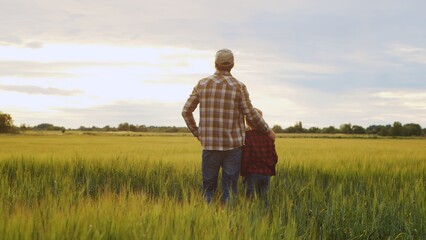 Fototapeta na wymiar Farmer and his son in front of a sunset agricultural landscape. Man and a boy in a countryside field. Fatherhood, country life, farming and country lifestyle.