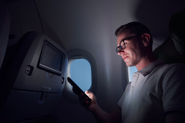 Man traveling by airplane. Passenger using phone during night flight..