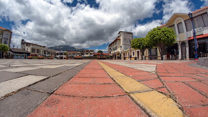 Tiles forming lines and checkerboard patterns on the ground in Ornamental Park in Cotacachi, Ecuador, taken with a fisheye lens, with a blue sky and white clouds above